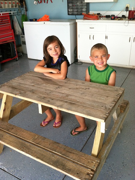 Two little kids sitting on a bench near a desk at a school environment.