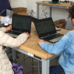 Two little kids are sitting on a table and learning on laptop.