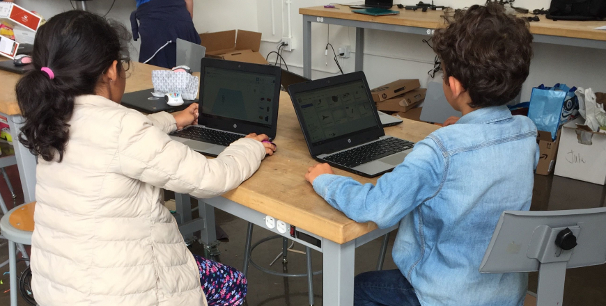 Two little kids are sitting on a table and learning on laptop.